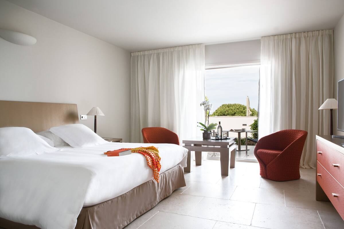 A hotel room with a bed, two chairs, a table, and a TV.