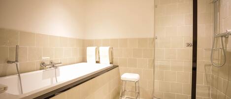 A modern bathroom with a glass-enclosed shower, a white bathtub, and a small stool.