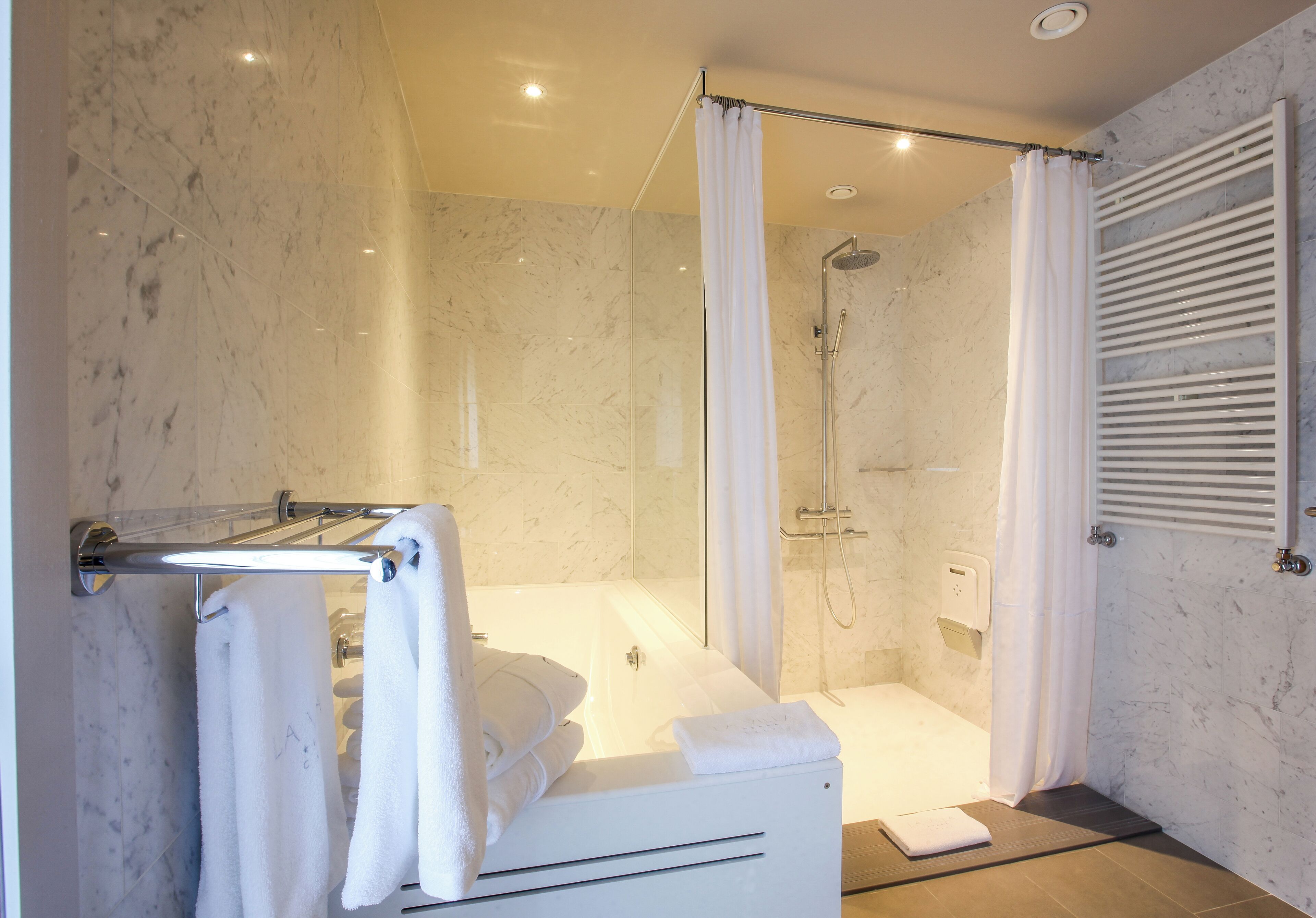 A modern bathroom with a glass-enclosed shower, a bathtub, and a towel rack with neatly folded towels.