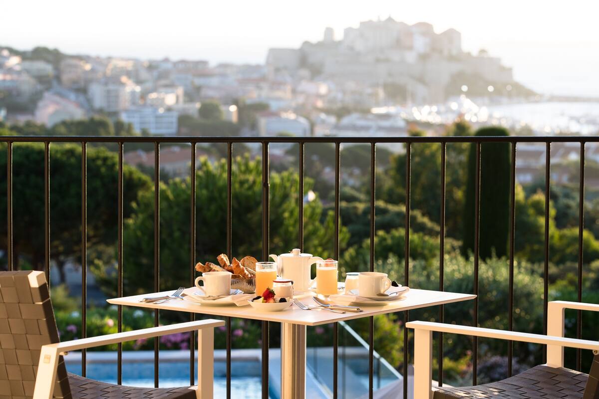 A balcony with a table set for breakfast, overlooking a cityscape and a body of water.