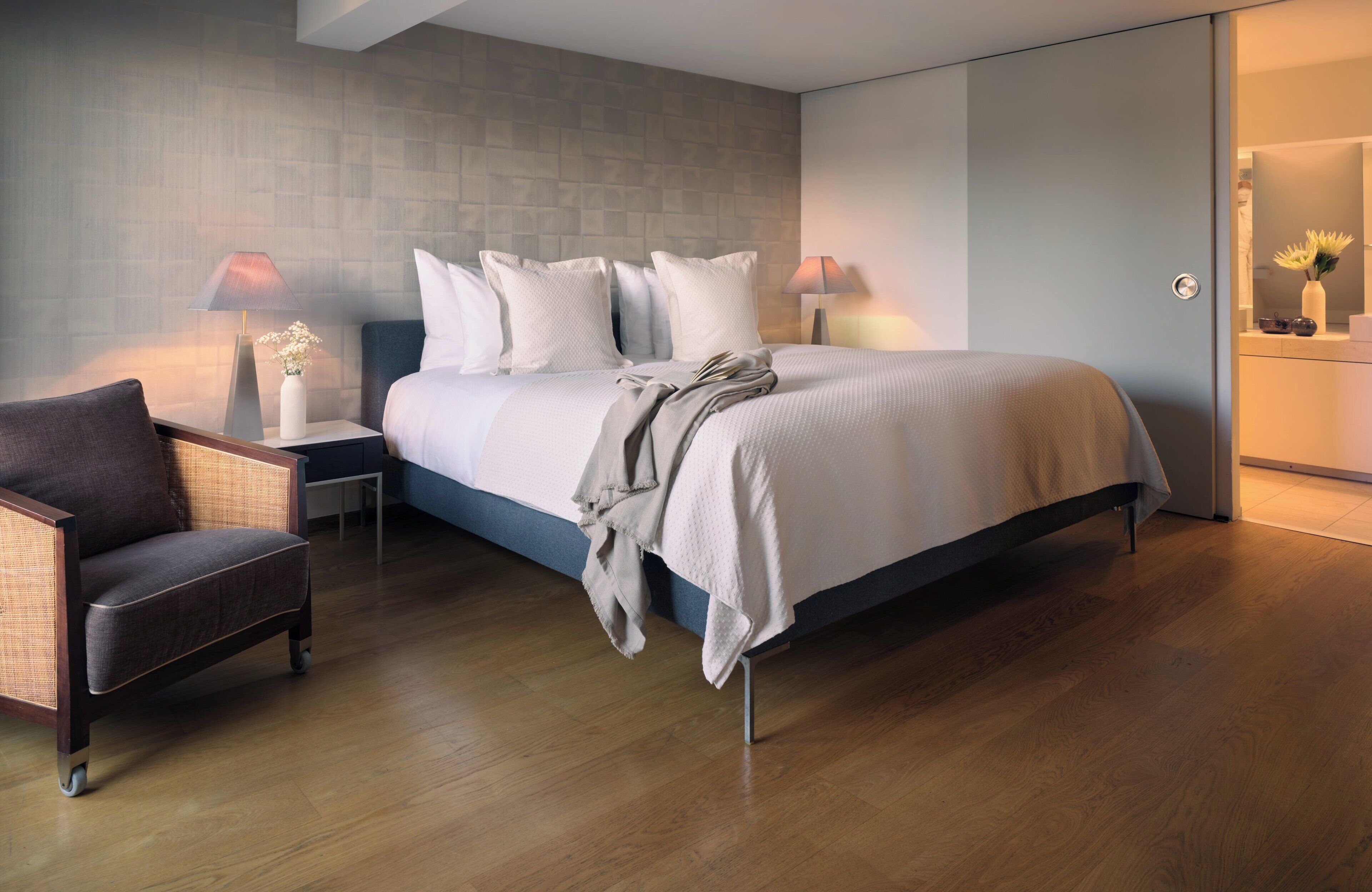 Un dormitorio moderno con una cama grande, dos mesitas de noche, una butaca y un espejo.