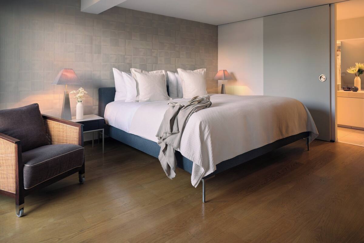 Ein modernes Schlafzimmer mit einem großen Bett, zwei Nachttischen, einem Beistelltisch, einem Sessel und einem Spiegel.