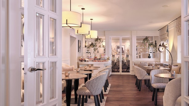 A dining area with round tables and patterned chairs, a white door with glass panels, and a ceiling with recessed lighting. - Hotel Alden Splügenschloss Zürich - Leonardo Limited Edition (Zürich)