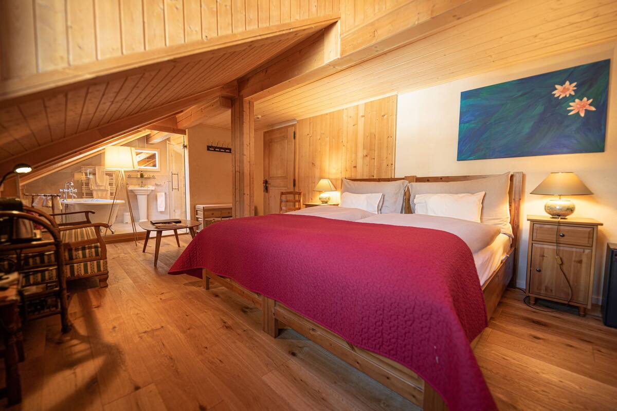 A cozy bedroom with a large bed, wooden walls, and a painting on the wall.