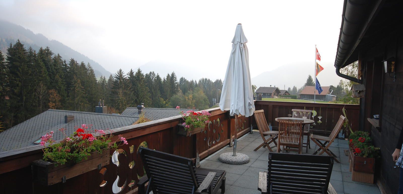 A wooden deck with outdoor seating, a covered umbrella, and a view of mountains.