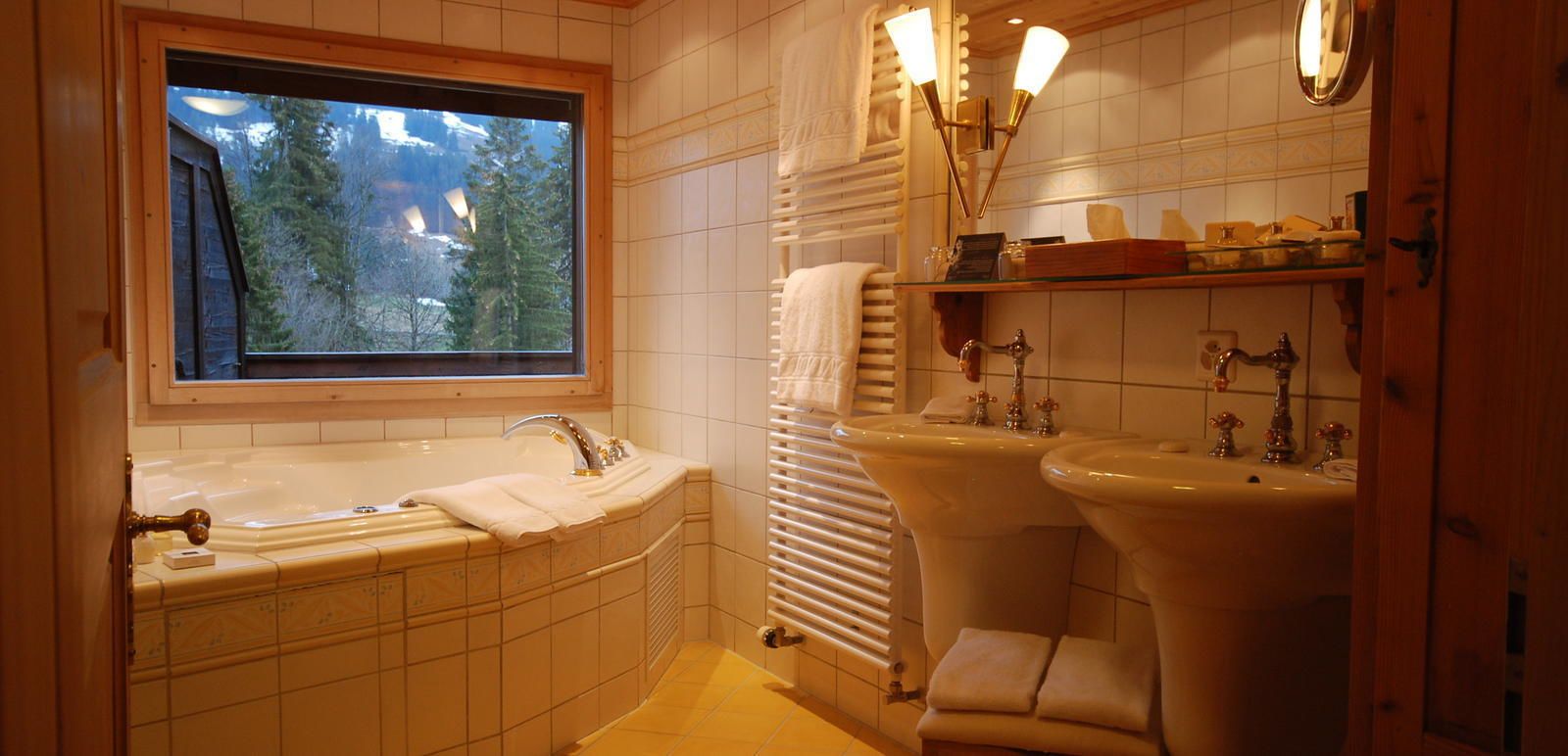 Un baño con bañera, dos lavamanos, una ventana con vistas a árboles y un perchero para toallas.