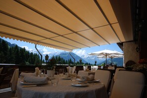 An outdoor dining area with tables set for two, overlooking a mountainous landscape.