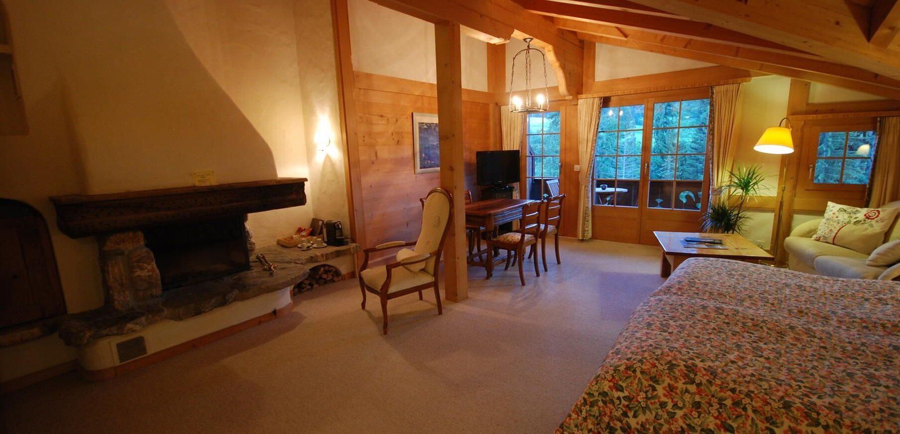 A cozy room with a fireplace, wooden furniture, a television, and large windows.