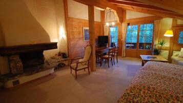 A cozy room with a fireplace, wooden furniture, a television, and large windows.