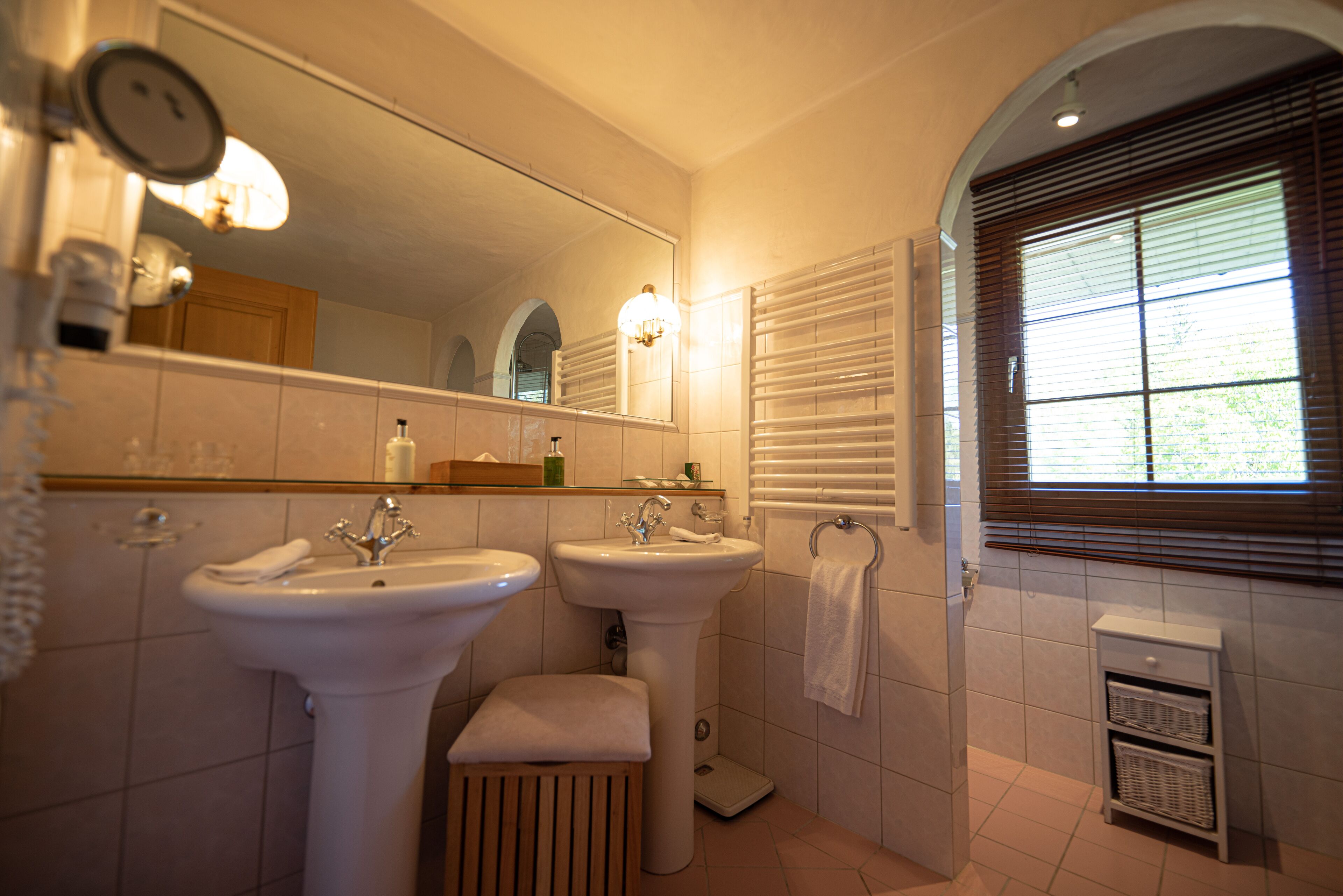 A bathroom with two sinks, a mirror, a towel rack, and a window with blinds.