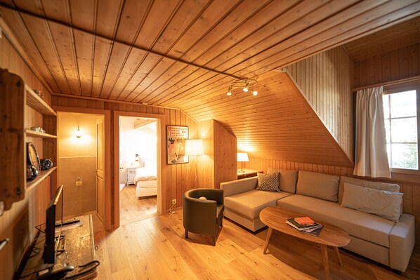 A cozy wooden cabin interior with a sofa, armchair, and a small table. A bathroom is visible in the background. - Boutique Hotel Alpenrose (Saanen)