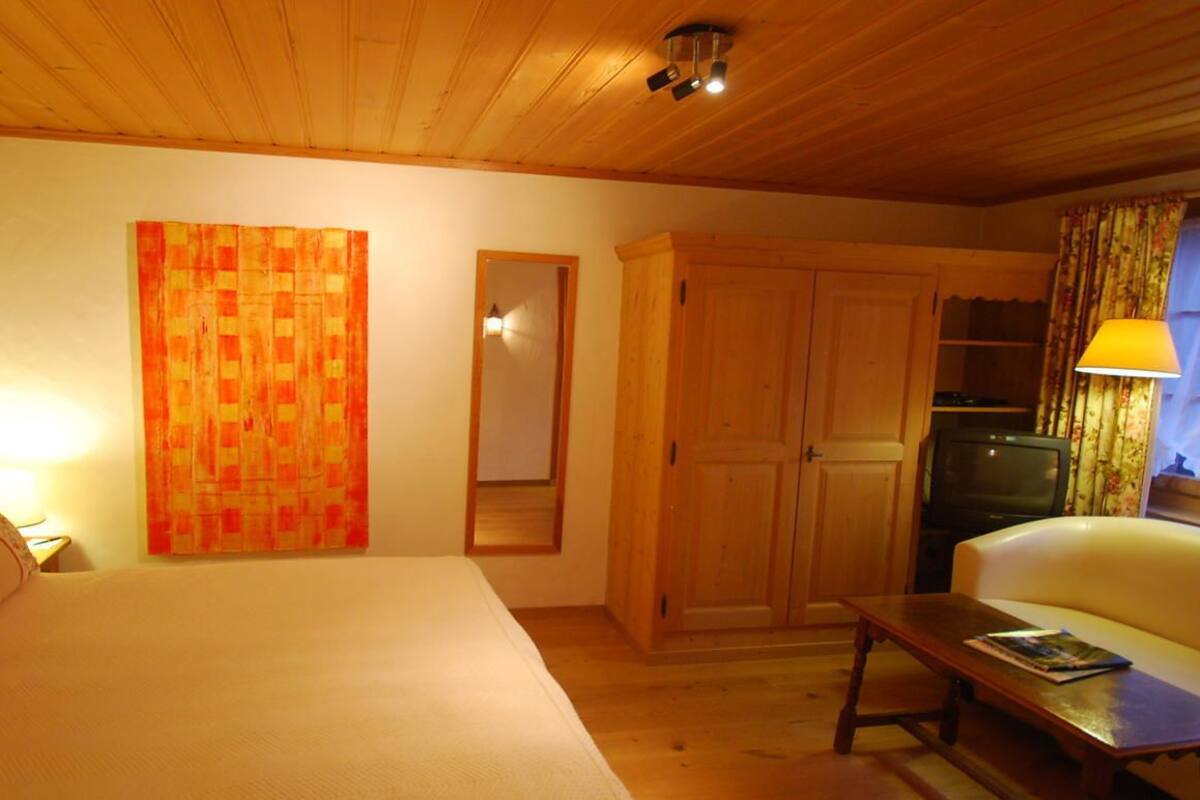 A cozy room with a bed, a wooden wardrobe, a television, and a table with a lamp.