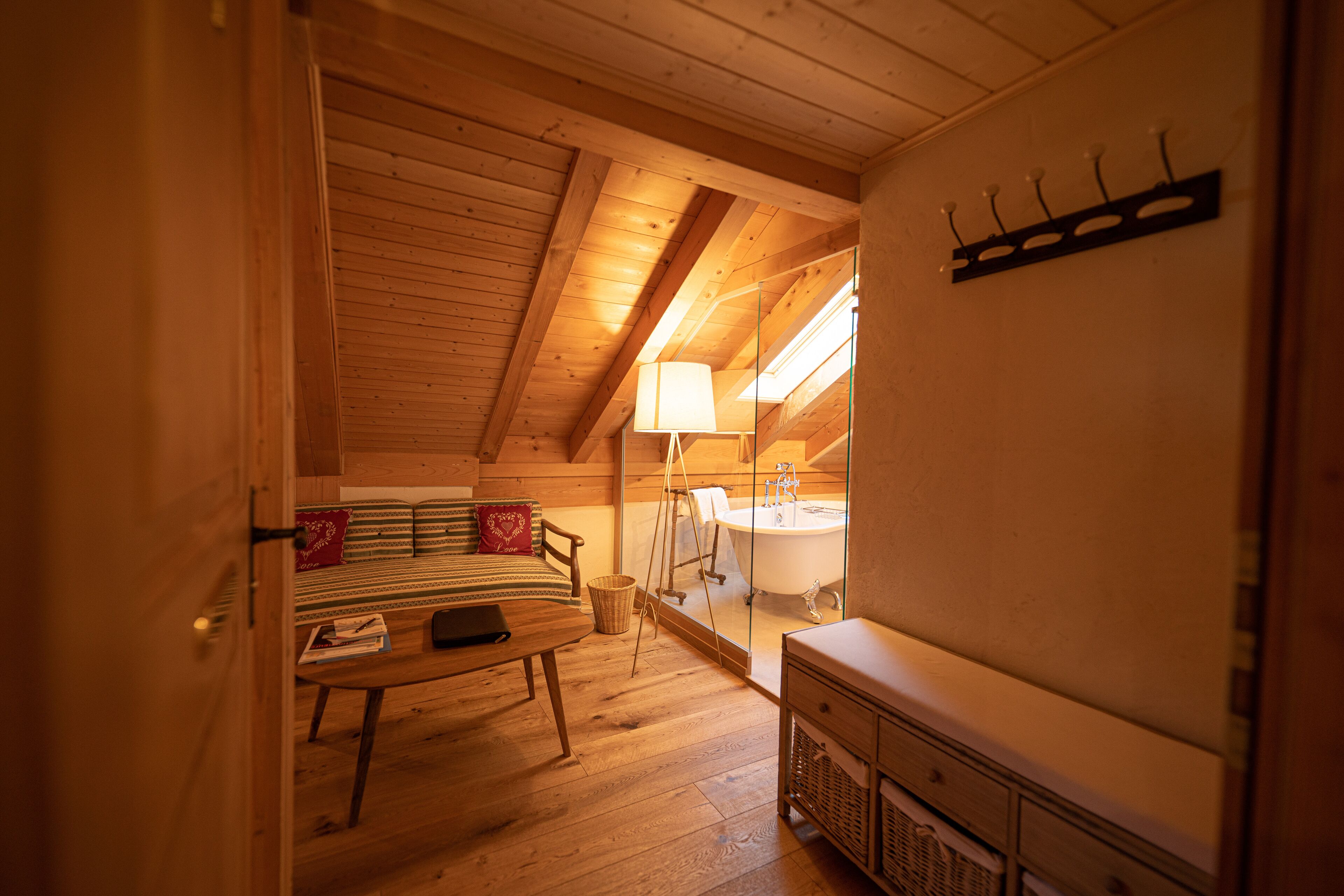 Una habitación acogedora de madera con cama, mesa, lámpara y baño con bañera y lavamanos.