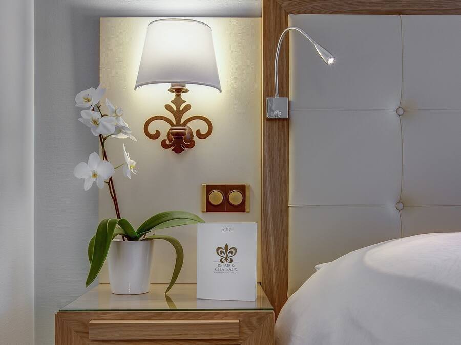 A neatly made hotel room with a bedside table, a lamp, a potted orchid, and a framed certificate.