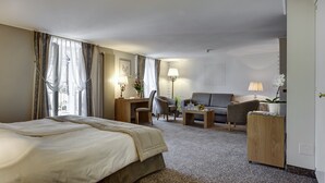 A hotel room with a large bed, a desk, a chair, a sofa, and a wardrobe. - Résidence Les Sources Des Alpes (Leukerbad)