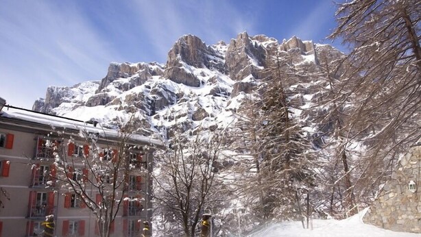 A hotel with a pool, snow-covered mountains in the background, and a clear sky. - Résidence Les Sources Des Alpes (Leukerbad)