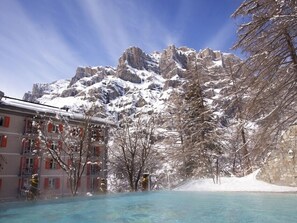 Un hotel con piscina, montañas nevadas al fondo y cielo despejado.