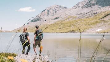 Two people hiking near a lake with mountains in the background.