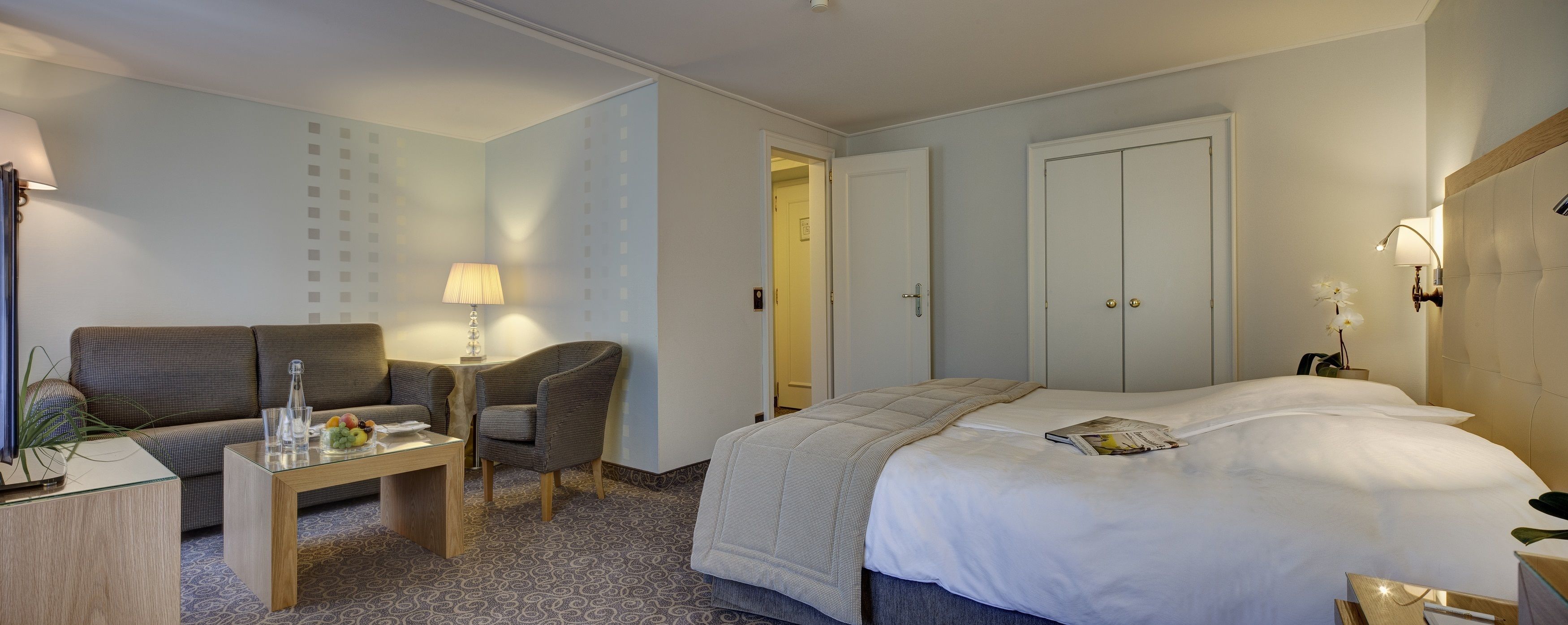 Une chambre d’hôtel avec un lit, un canapé, une petite table avec une lampe et une chaise.