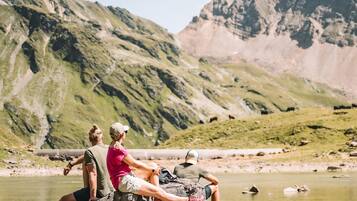Un couple est assis sur des rochers, au bord d’une rivière paisible, avec des montagnes en arrière-plan.