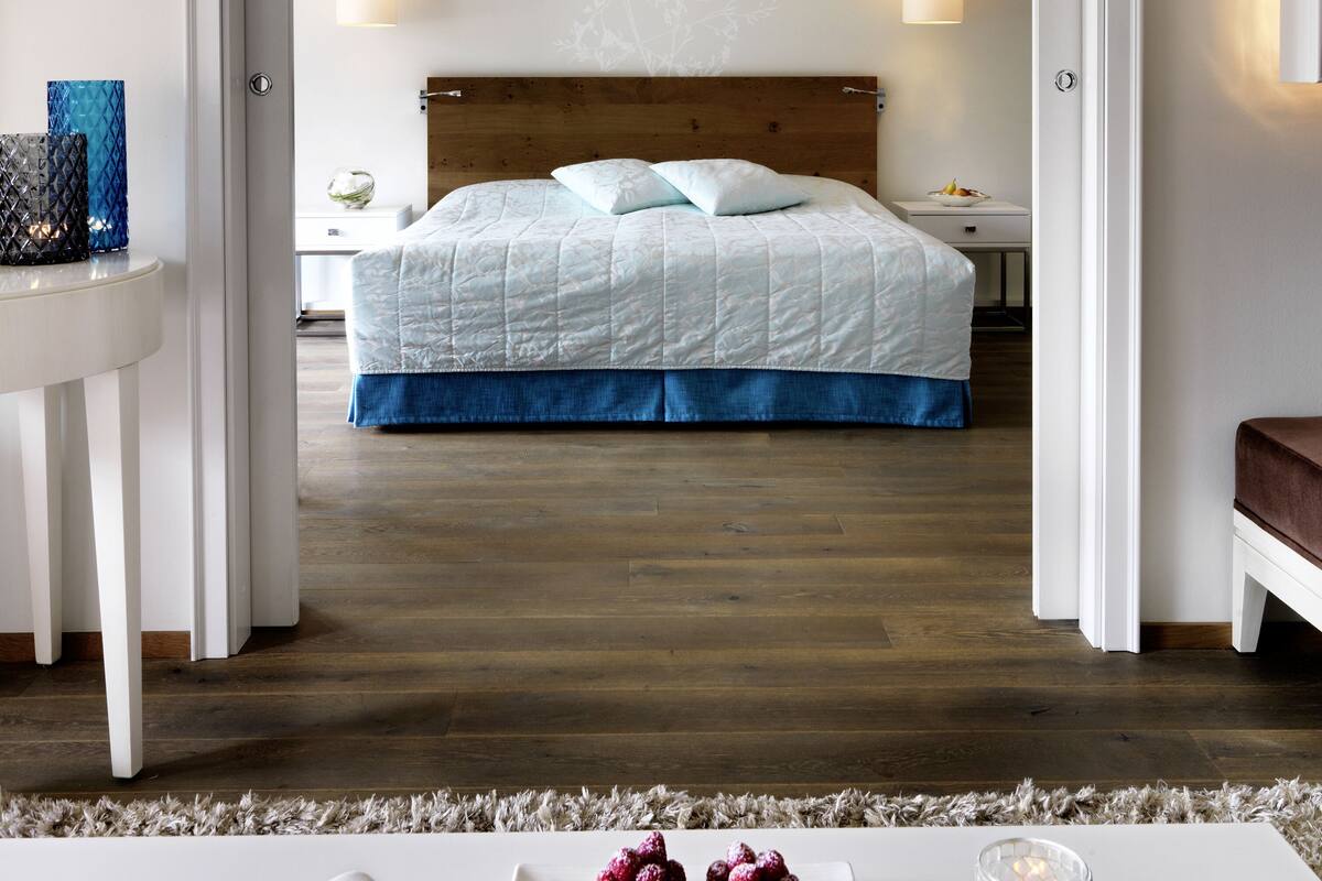 A hotel room with a bed, bedside tables, a nightstand, and a view through an open door.