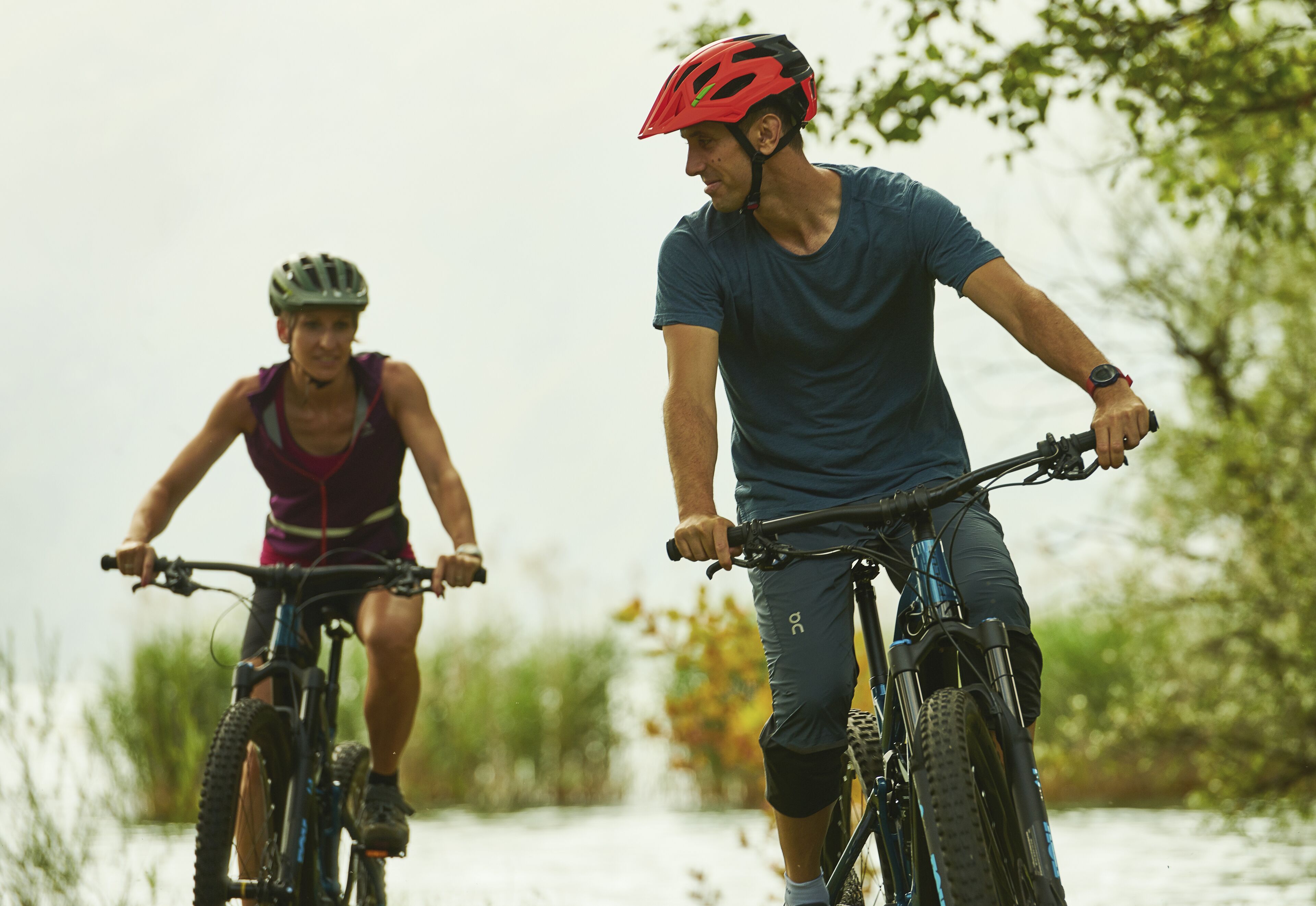 Two cyclists on a bike path with trees and water in the background.