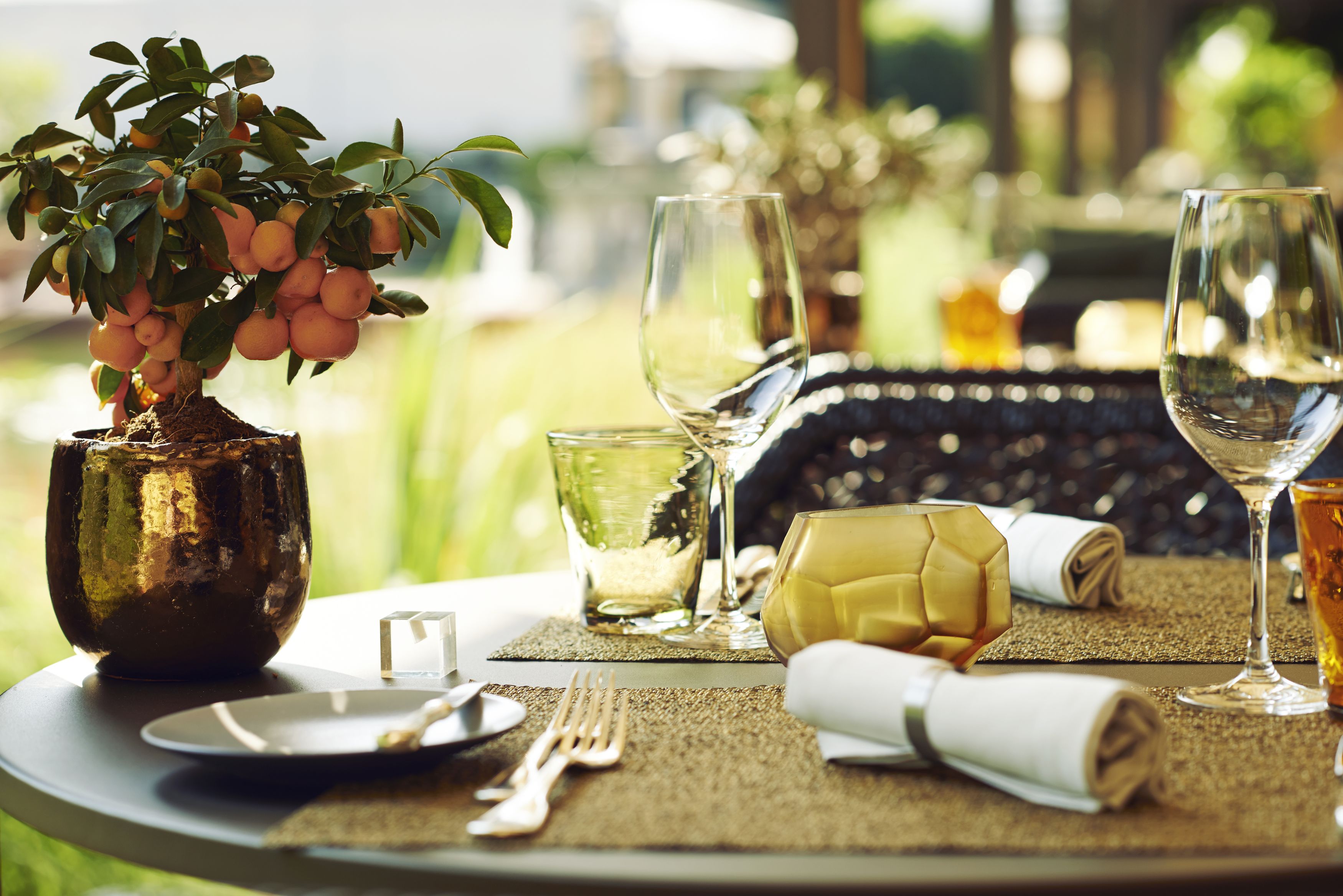 A dining table set with a vase of fruit, wine glasses, and cutlery.