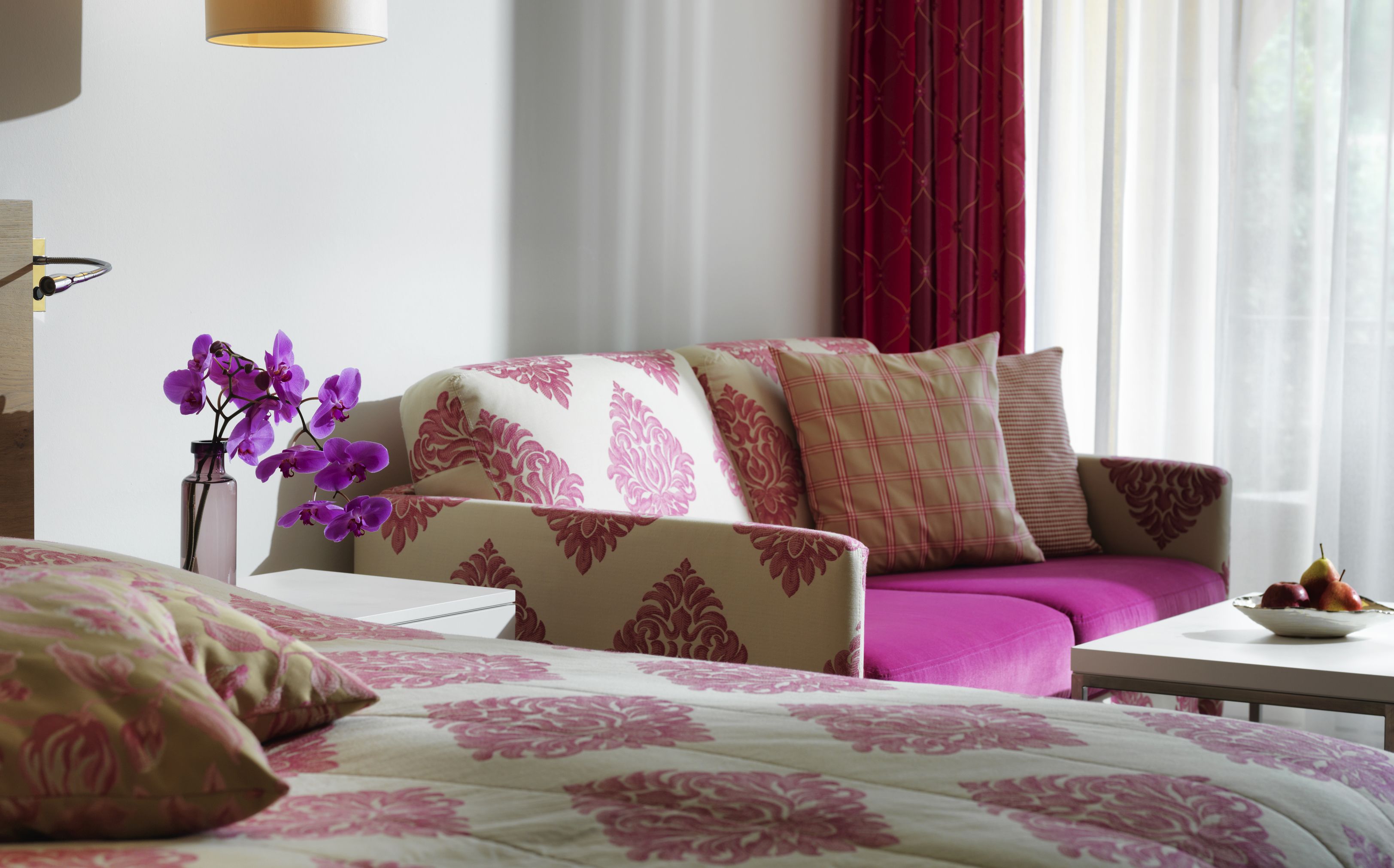 Une chambre d’hôtel avec un lit, un canapé, une table avec des fruits et un vase rempli de fleurs.