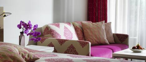 Une chambre d’hôtel avec un lit, un canapé, une table avec des fruits et un vase rempli de fleurs.