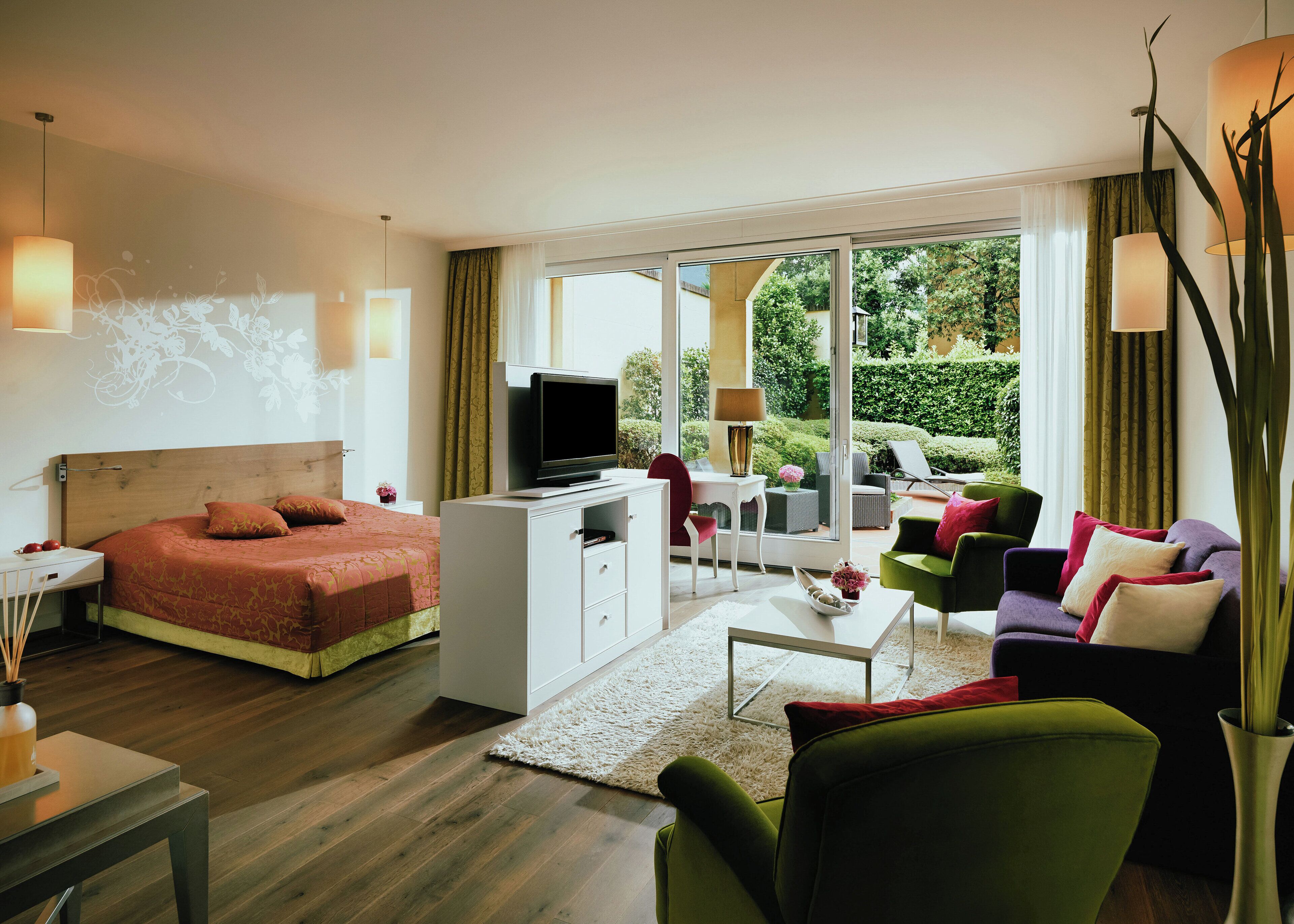 Una habitación de hotel moderna con cama, televisor, escritorio, sofá y balcón con vistas a zonas verdes.