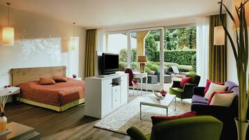 Una habitación de hotel moderna con cama, televisor, escritorio, sofá y balcón con vistas a zonas verdes.