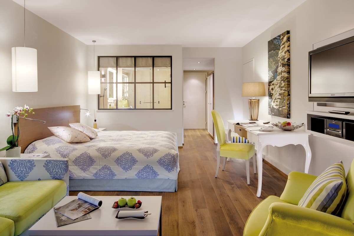 A hotel room with a bed, two chairs, a desk, a television, and a window.
