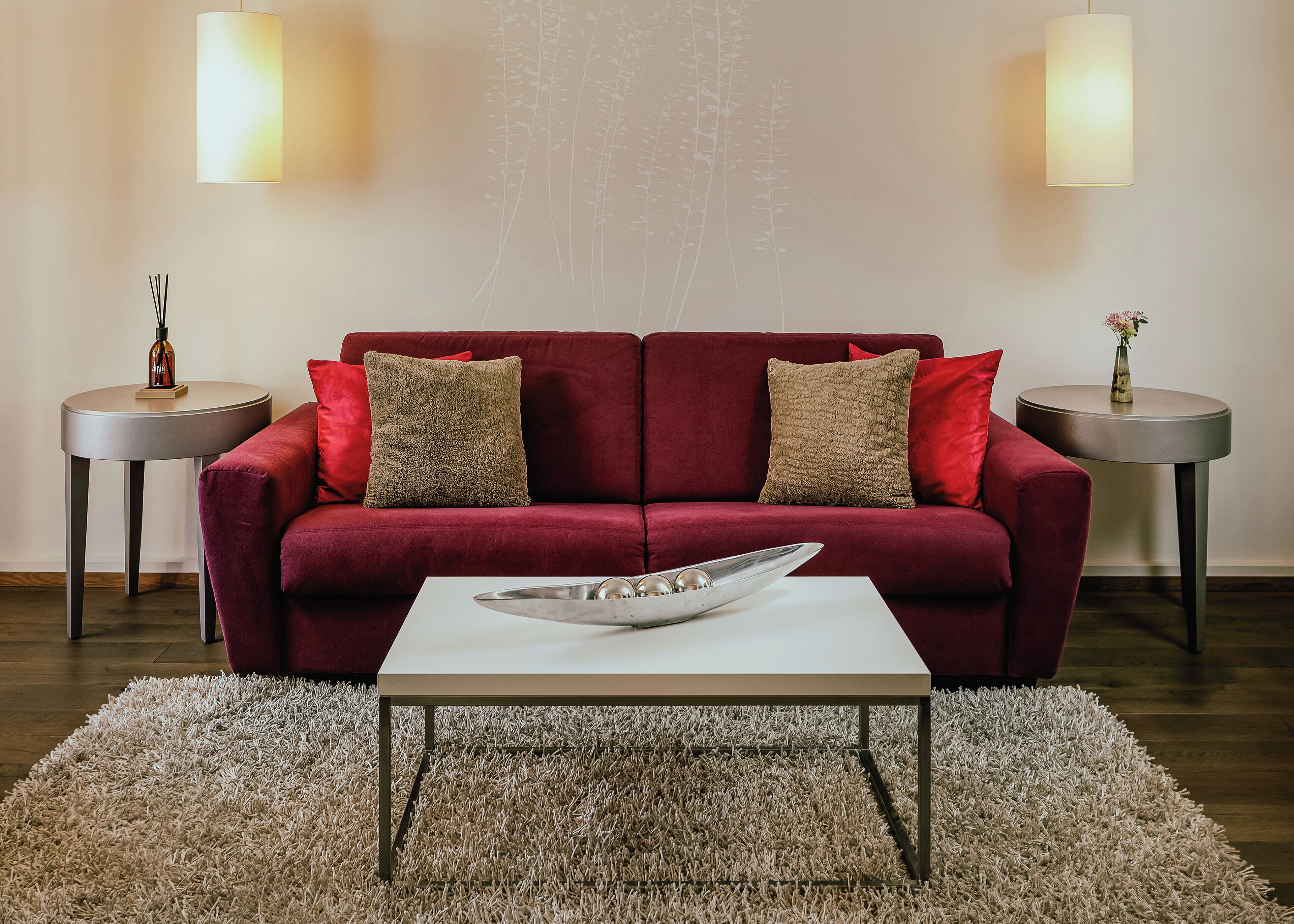 A red sofa with two cushions, a white coffee table, and two side tables with decorative items.