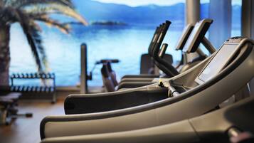 A gym with exercise equipment and a large window overlooking a body of water.