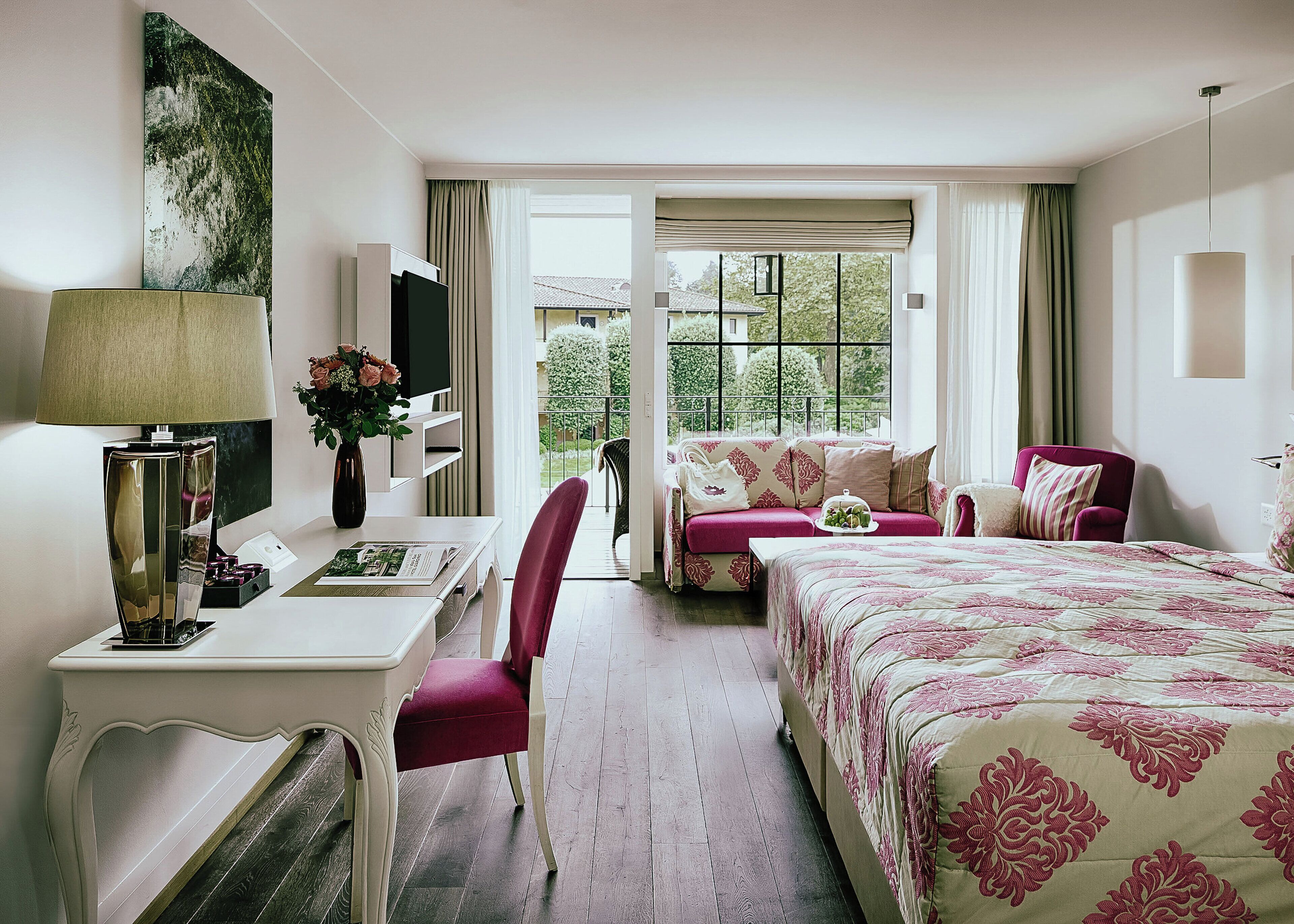 Habitación de hotel con cama, escritorio, sillón, sofá y ventana con vistas a zonas verdes.
