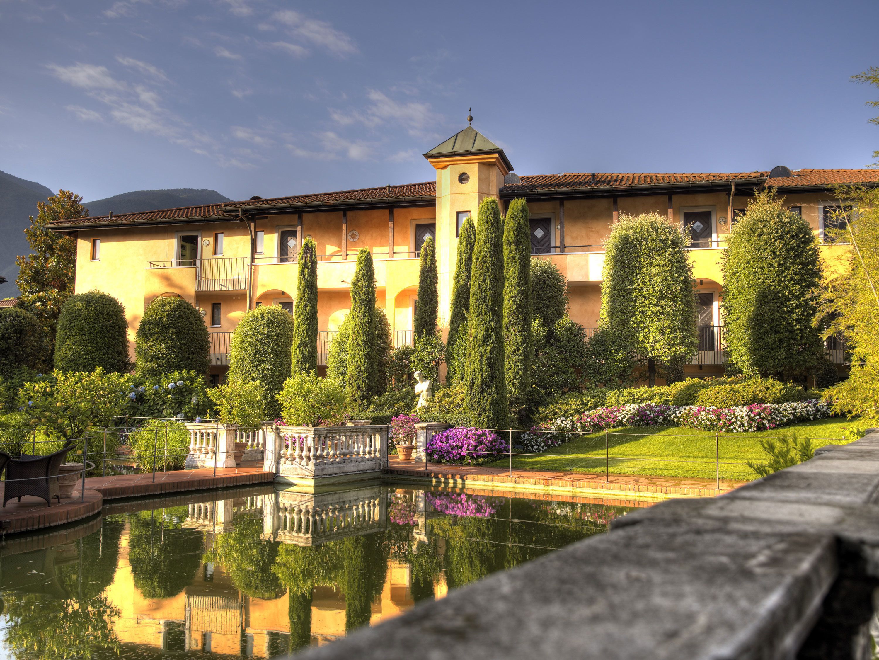 A large building with a central tower, surrounded by manicured gardens and a reflecting pool.