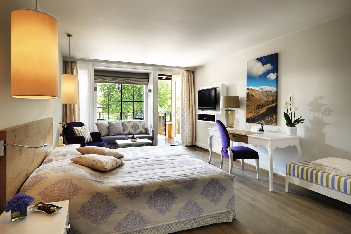 A hotel room with a large bed, a desk, a chair, a TV, and a window with a view of the outdoors.