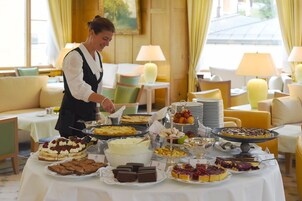 A buffet table with various desserts and a person serving food.