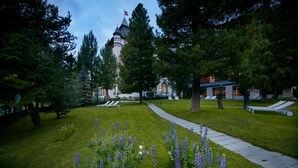 A well-maintained garden with a pathway, benches, and a building with a tower in the background. - Hotel Walther (Pontresina)