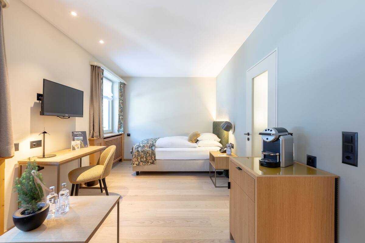 Ein modernes Hotelzimmer mit Bett, Schreibtisch, Stuhl, Fernseher und einer Kaffeemaschine.