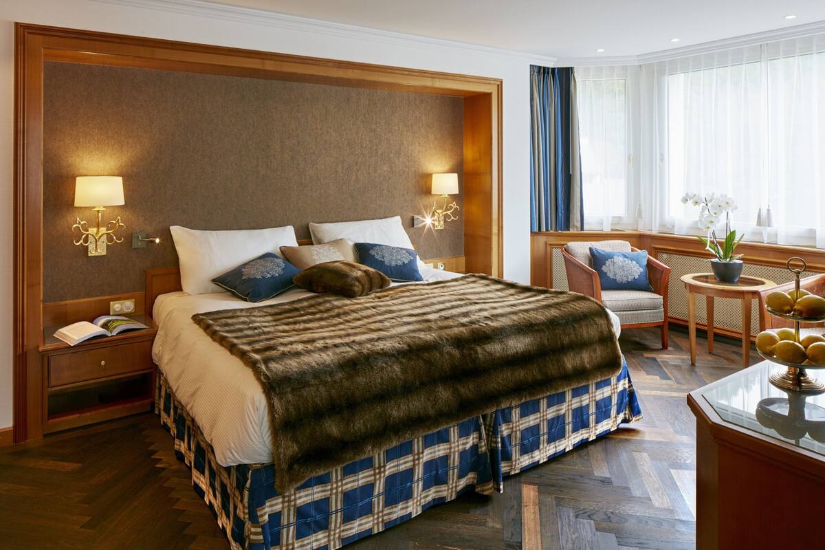 Ein Hotelzimmer mit einem großen Bett, zwei Nachttischlampen, einem Holz-Kopfteil, einem kleinen Tisch mit einer Vase und einem Sessel.