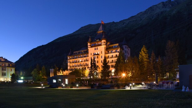 A large, multi-story hotel with a prominent tower and flag, surrounded by a well-lit courtyard and trees. - Hotel Walther (Pontresina)
