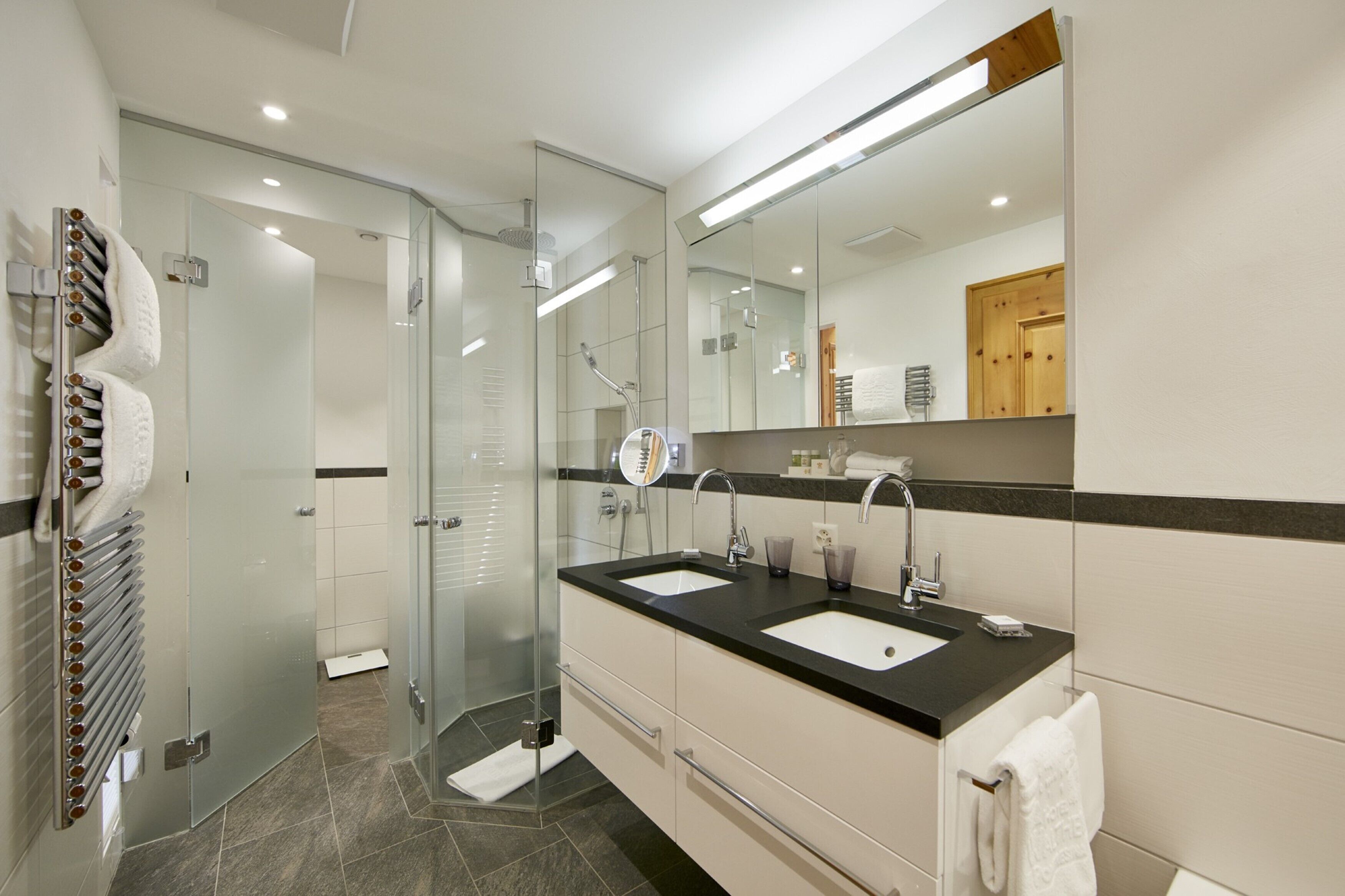 Une salle de bain moderne avec une douche à l’italienne en verre, deux vasques et un grand miroir.
