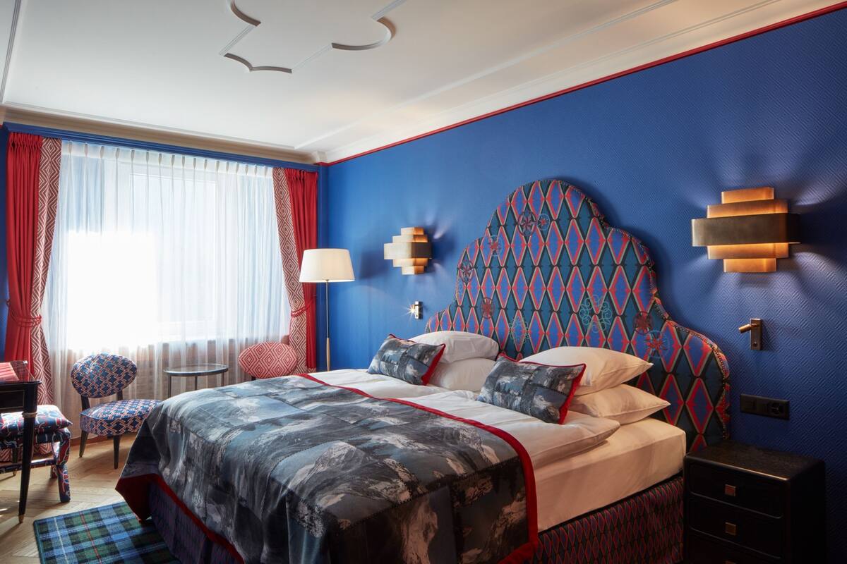 Ein modernes Schlafzimmer mit blauer Akzentwand, einem gemusterten Kopfteil und einem Bett mit roter und schwarzer Bettdecke.