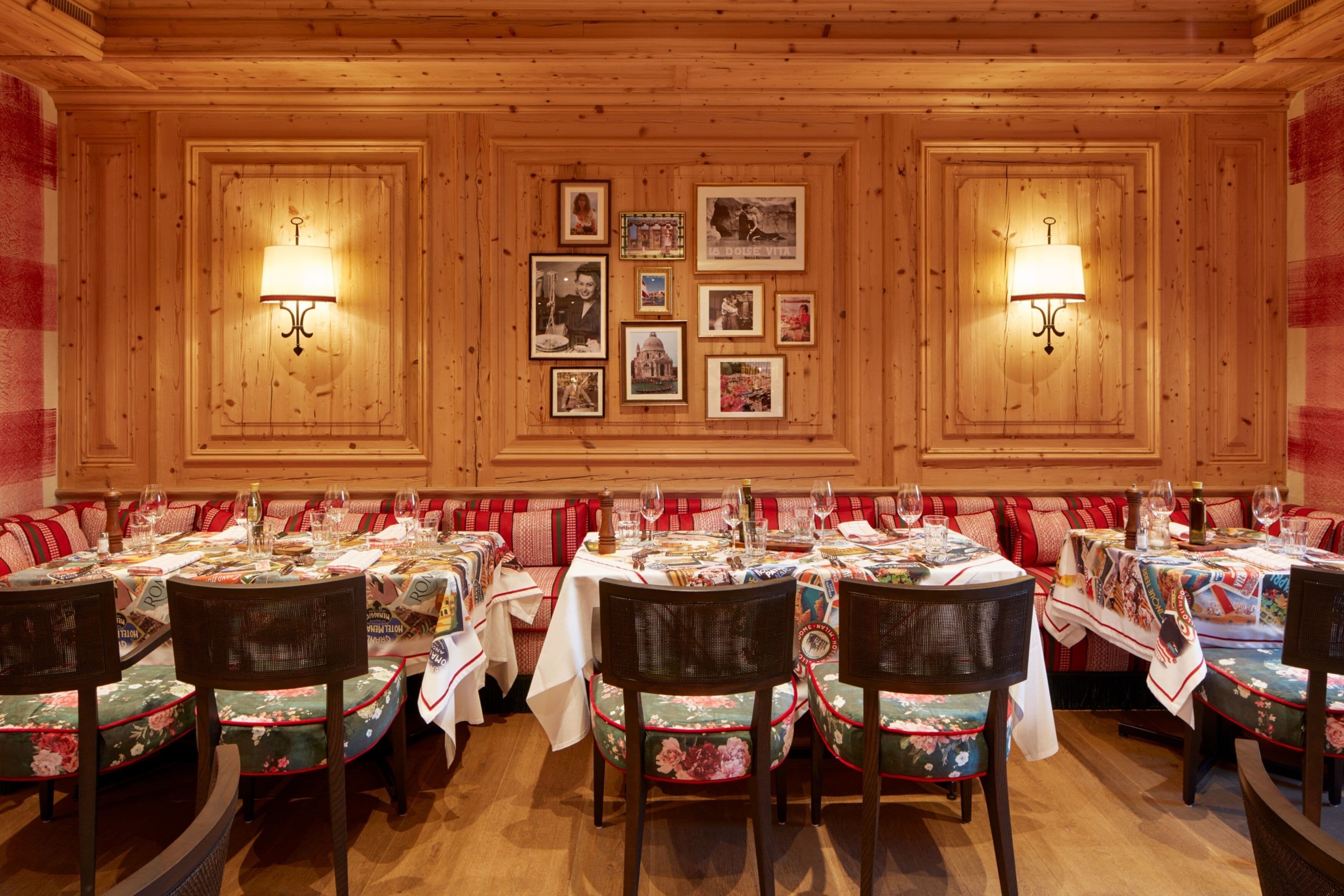 Ein Restaurant mit Holzwänden, gerahmten Bildern und gedeckten Tischen, komplett mit Weingläsern und Tellern.