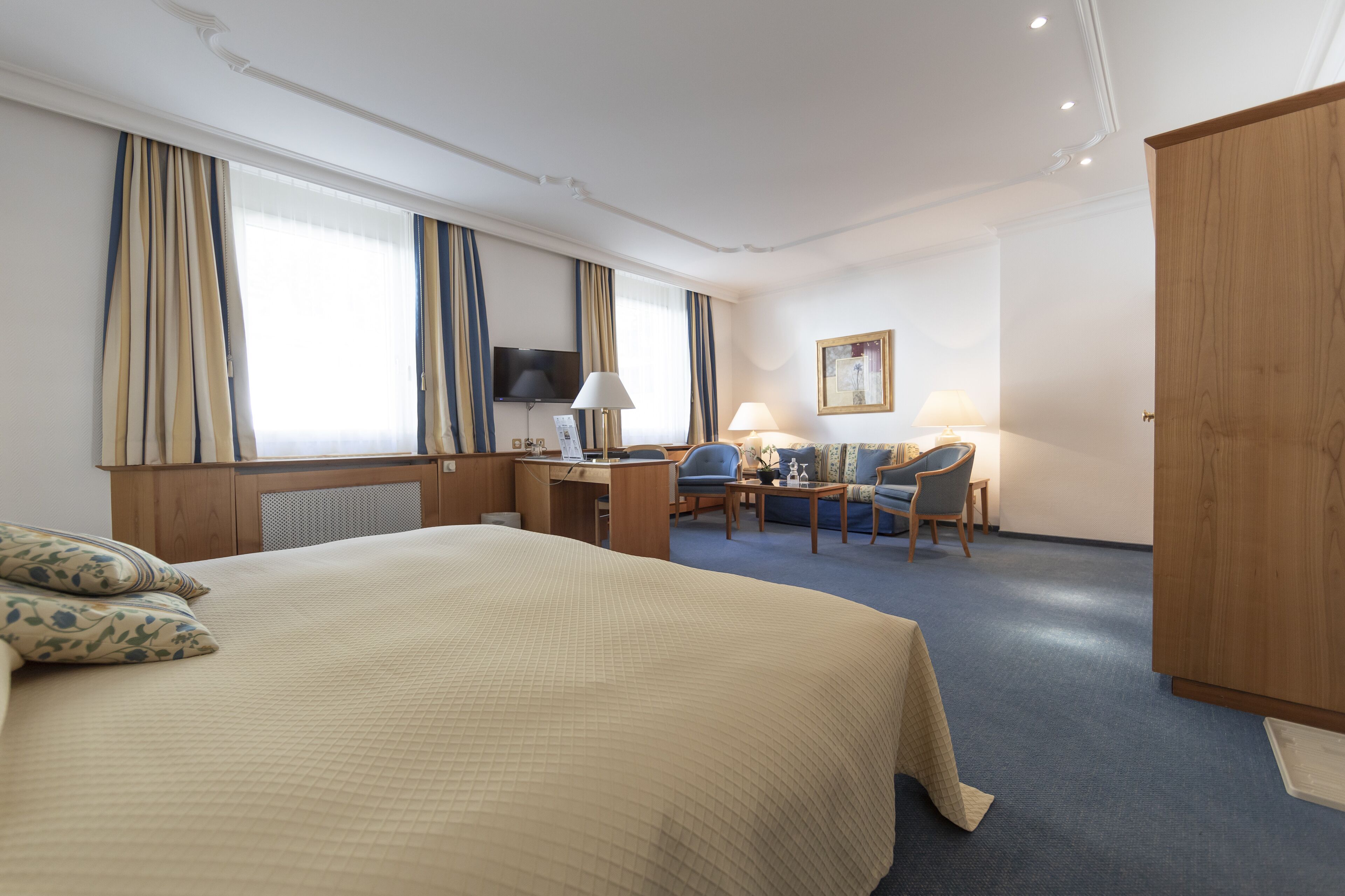 Habitación de hotel con una cama grande, un escritorio con computadora, una silla, televisor y armario.