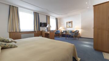 Habitación de hotel con una cama grande, un escritorio con computadora, una silla, televisor y armario.