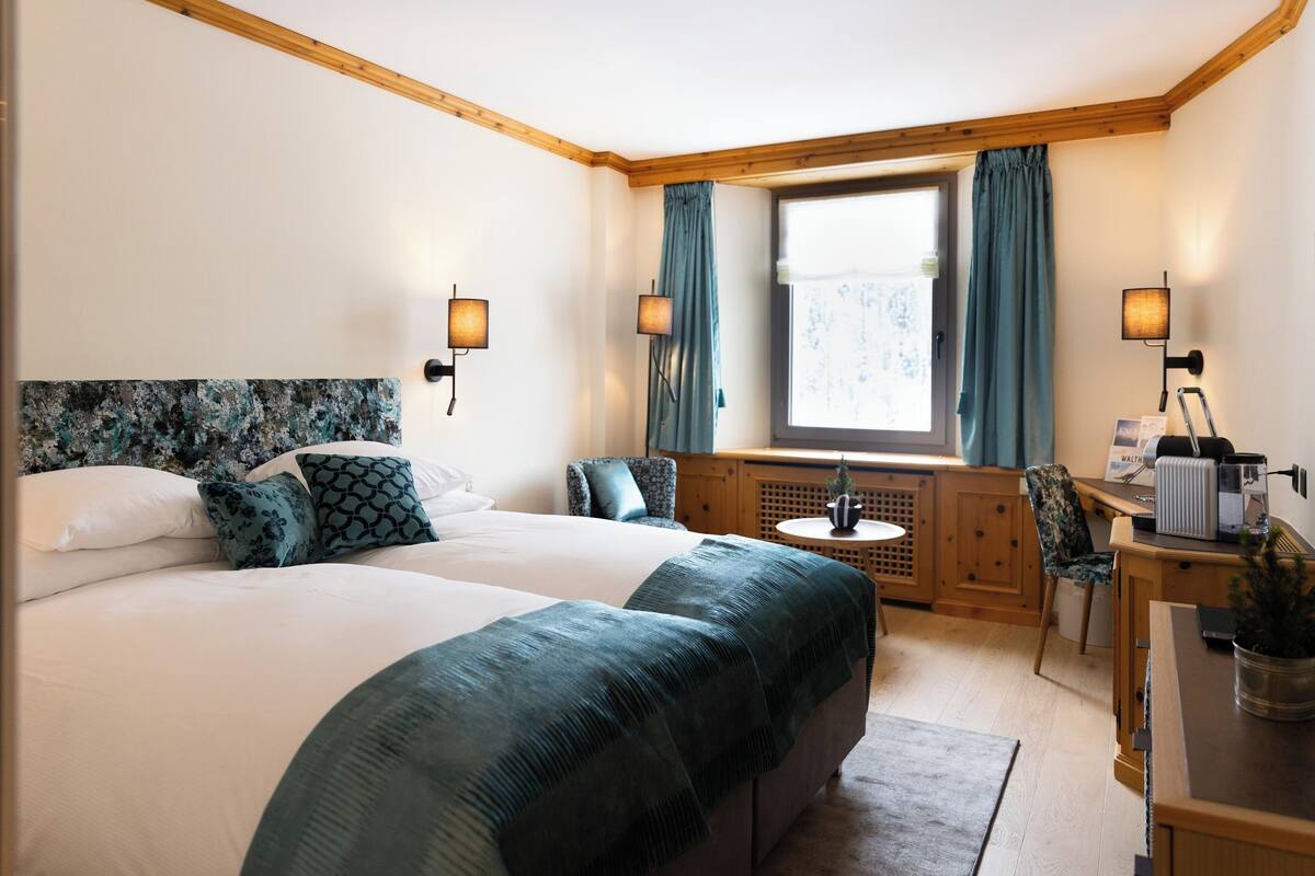Ein Schlafzimmer mit einem großen Bett, zwei Nachttischen, einem Fenster mit Vorhängen, einem kleinen runden Tisch und einem Stuhl.