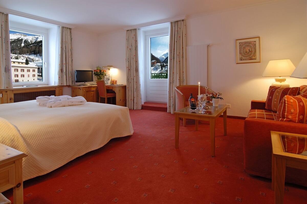 Ein Hotelzimmer mit Bett, Schreibtisch mit Computer, Stuhl, Tisch mit Lampe und Sofa.