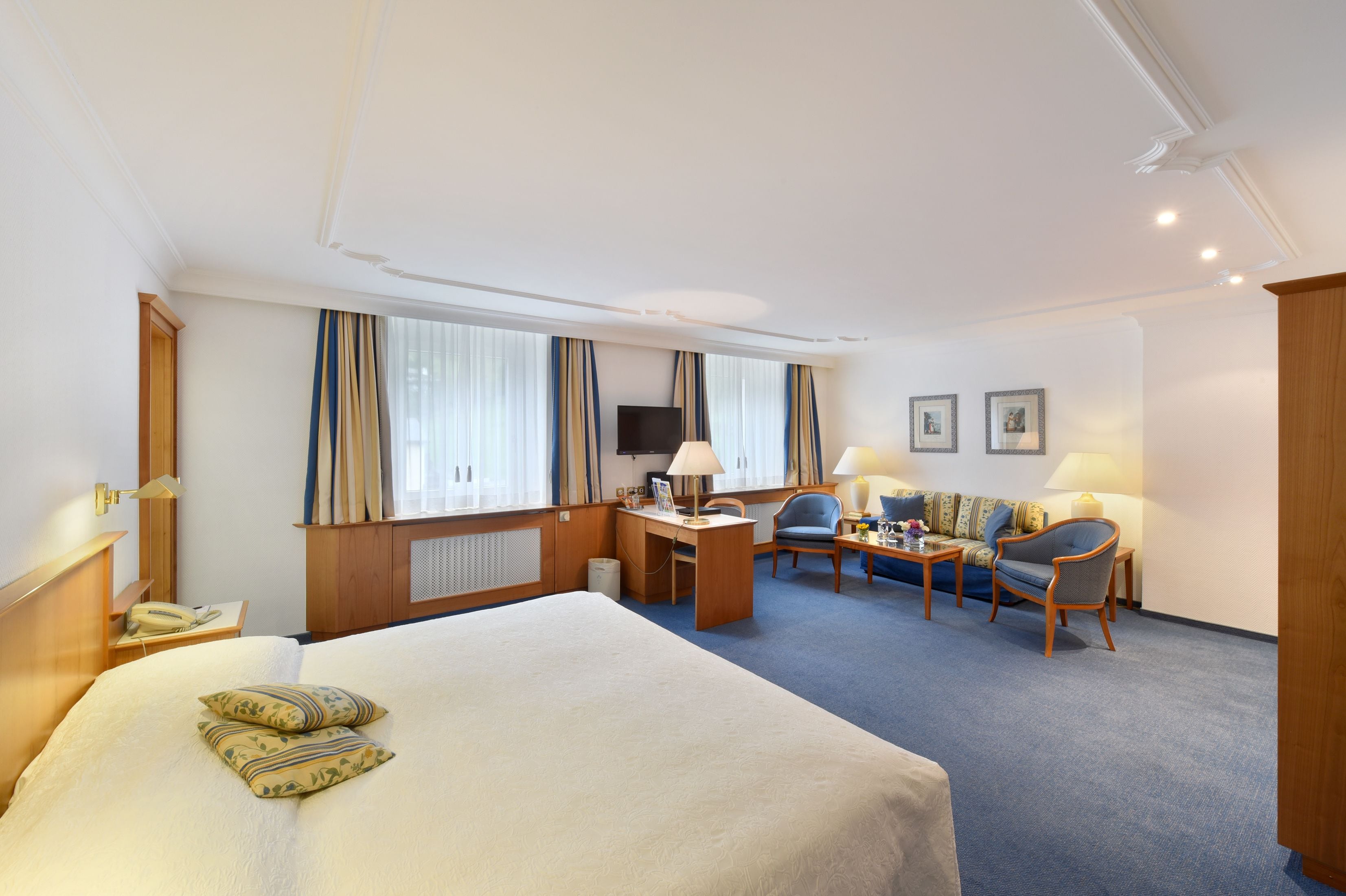 A hotel room with a large bed, a desk with a chair, a sofa, and a television.
